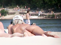 Hot bronze skin blonde is wearing nothing but the cap that is hiding her head from the heating sun in the middle of the nudist beach