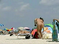 Naked nudist is lying on the beach and getting her beautiful clean shaven pussy suntanned.