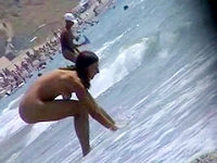 The charming naked girls are entertaining in the warm waves of the ocean.